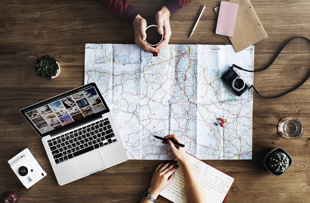 Pessoas a planear uma viagem sobre um mapa, com portátil, caderno e café numa mesa